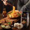 Person eating pad thai with a bottle and package of SIAM Pad Thai Rice Noodles on a wooden table.